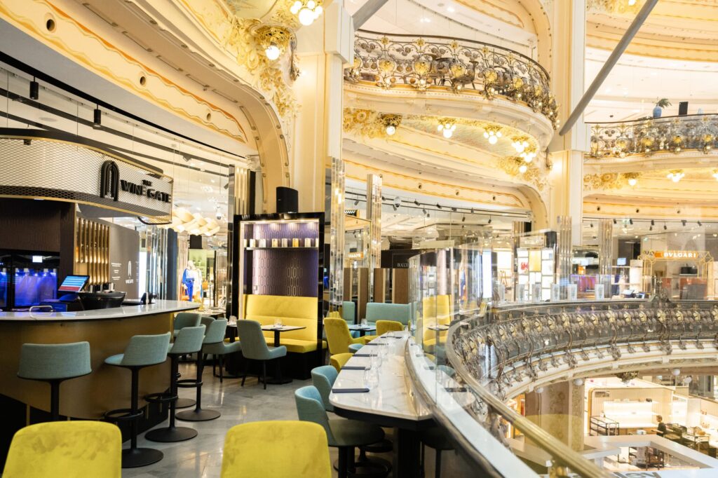 le forum du rotary un café aux chaises jaunes et sarcelles se trouve à l'intérieur d'un centre commercial orné de décorations dorées, de rampes en verre et de lumières vives un cadre parfait pour une expérience de la mode française. des étalages et des vitrines sont visibles à l'arrière plan.