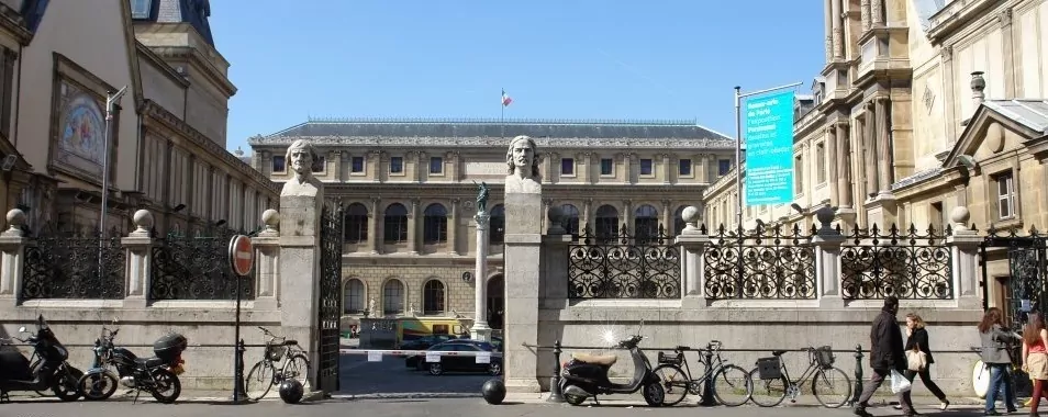 le forum du rotary un portail historique en fer orné de piliers en pierre et de deux statues en buste se dresse devant un grand bâtiment classique arborant le drapeau français. plusieurs bicyclettes sont garées à proximité, tandis que des personnes marchent sur le trottoir, peut être à la recherche d'informations pratiques à l'intérieur.