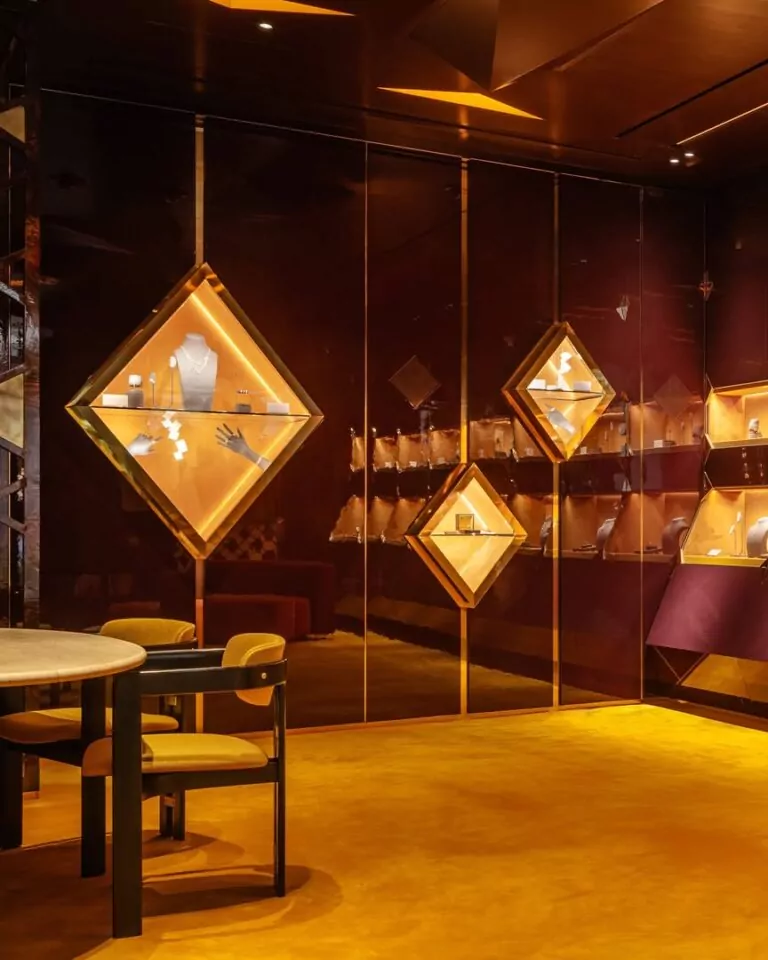 le forum du rotary une salle d'exposition moderne avec des vitrines éclairées en forme de diamant sur un mur sombre et brillant, mettant en valeur des bijoux sur des supports. il y a également des étagères avec d'autres articles et une table ronde avec des chaises au premier plan.