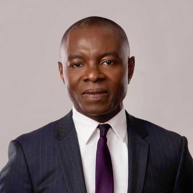 le forum du rotary un homme portant un costume à rayures sombres, une chemise blanche et une cravate mauve foncé pose sur un fond gris clair uni. il regarde directement la caméra avec une expression neutre.