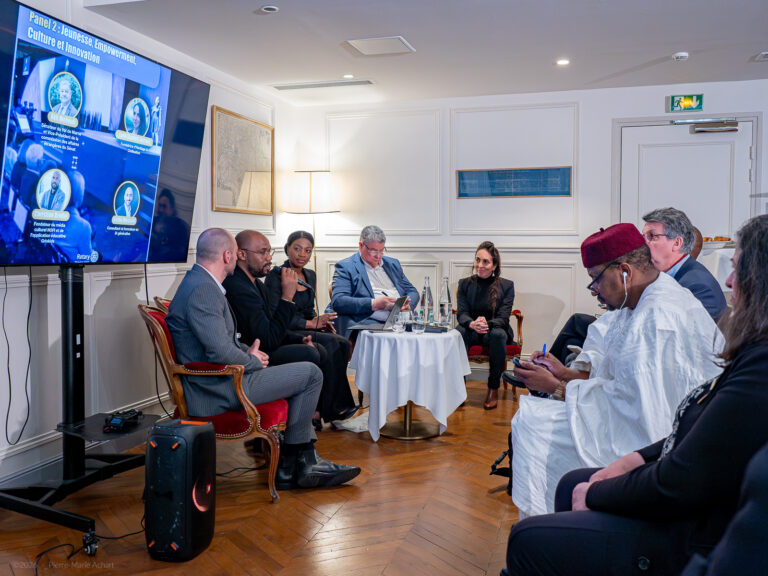 le forum du rotary un groupe de personnes est assis en demi cercle dans une salle bien éclairée et participe à un débat d'experts. un grand écran affiche les noms et les photos des participants. certaines personnes prennent des notes tandis que d'autres écoutent.