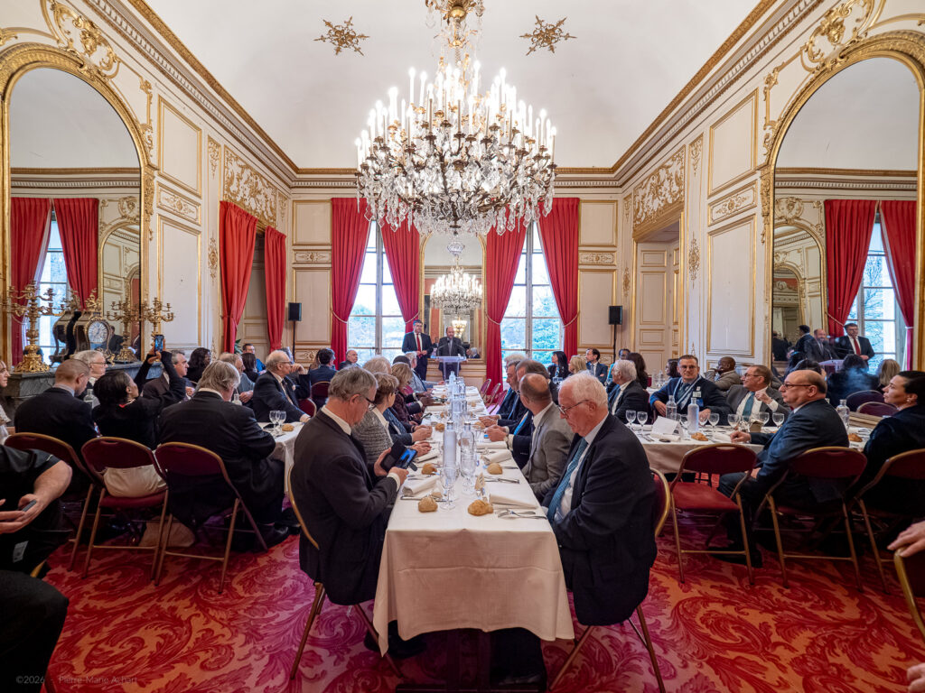le forum du rotary un dîner formel avec des personnes assises à de longues tables dans une salle ornée de lustres, de rideaux rouges, de détails dorés et d'un orateur debout à l'extrémité qui s'adresse aux participants.