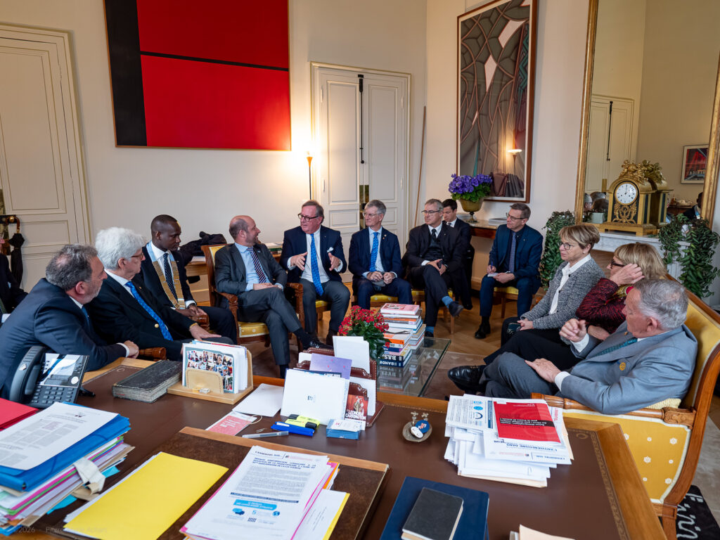 le forum du rotary un groupe de dix personnes en tenue de travail est assis dans un bureau formel et discute. des papiers et des livres recouvrent le bureau au premier plan. des œuvres d'art moderne, une horloge et un miroir sont visibles à l'arrière plan.