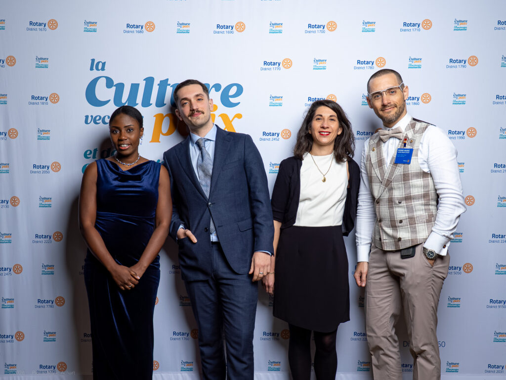 le forum du rotary quatre personnes en tenue de soirée se tiennent devant une banderole en escalier portant les logos du rotary et de la manifestation. elles posent pour une photo de groupe et sourient à l'appareil.