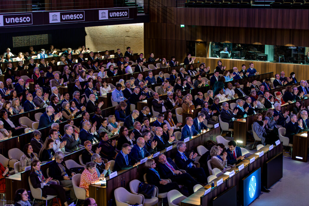 le forum du rotary un large public est assis dans un auditorium, regardant attentivement une présentation ou un événement. le lieu affiche plusieurs panneaux de l'unesco au dessus des places assises. la plupart des participants sont assis, certains applaudissent.