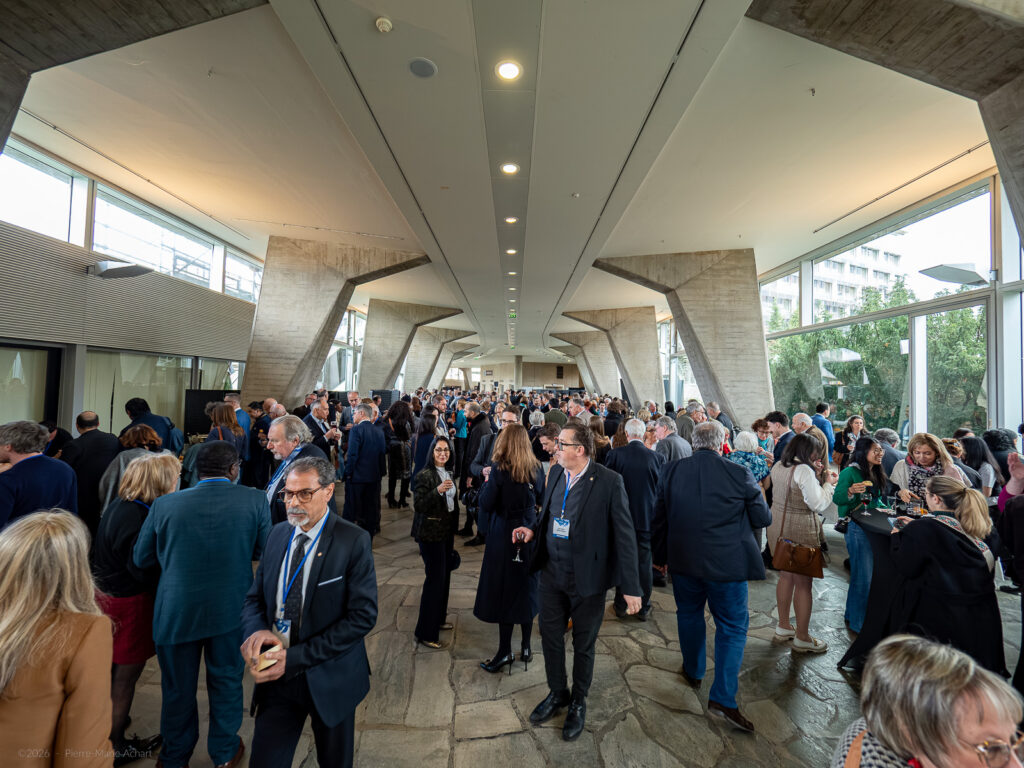 le forum du rotary un grand groupe de personnes en tenue de travail se réunit et socialise dans un couloir spacieux et moderne avec des colonnes en béton et des murs en verre lors d'un événement professionnel ou d'une conférence.