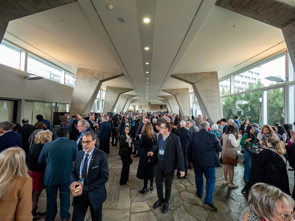 le forum du rotary un grand groupe de personnes en tenue de travail se réunit et socialise dans un couloir spacieux et moderne avec des colonnes en béton et des murs en verre lors d'un événement professionnel ou d'une conférence.