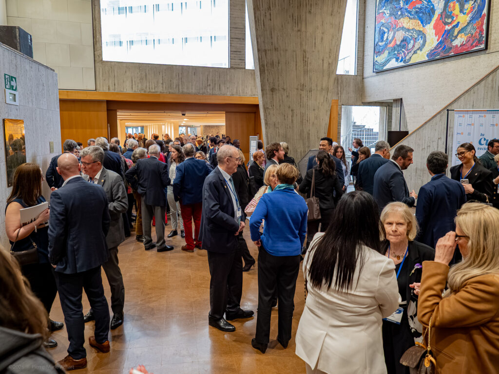 le forum du rotary un grand groupe de personnes en tenue de travail est rassemblé dans un hall d'entrée ou un couloir bien éclairé et discute. des œuvres d'art moderne sont exposées au mur et de grandes fenêtres laissent entrer la lumière naturelle.